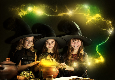 Three little Halloween witches reading conjure from magic bookの写真素材