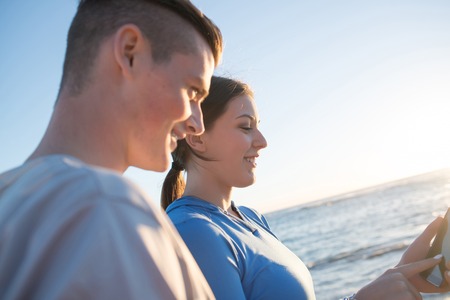 Young active couple of joggers on beach checking timeの写真素材