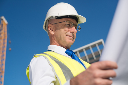 Construction engineer in hardhat making notes in blueprintの写真素材