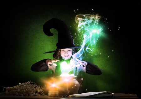 Little Halloween witch reading conjure from magic book above potの写真素材