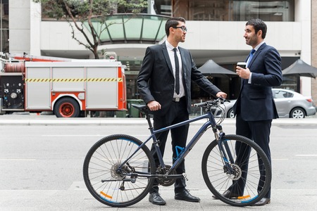 Businessmen talking while walking with bicycle outdoors