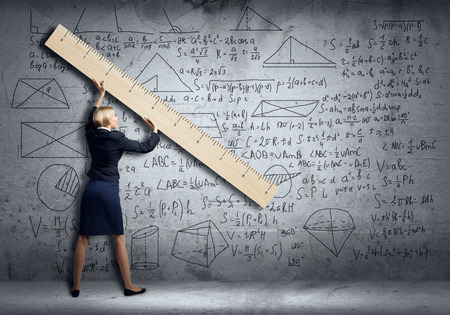 Young woman at blackboard measuring something with big rulerの写真素材