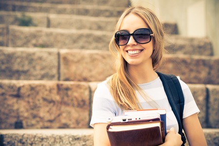 Smiling college student sitting on staircase and studying with booksの写真素材
