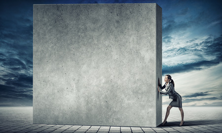 Young businesswoman making effort to move cement wallの写真素材