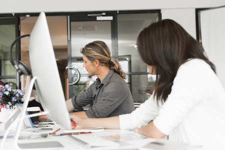 Young coworkers working together and discussing points while using computerの写真素材