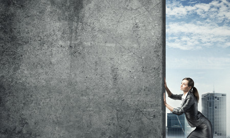 Young businesswoman making effort to move cement wallの写真素材