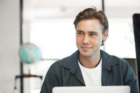 Young man in casual sitting at desk and working on computerの写真素材