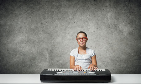 Cute school girl in red glasses playing pianoの写真素材