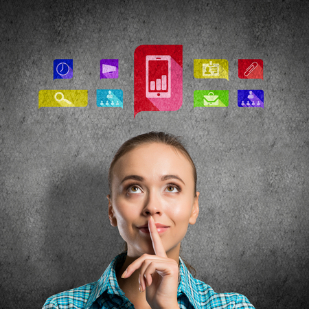 Portrait of attractive teenage girl with finger on lips on concrete background and application icons above headの写真素材