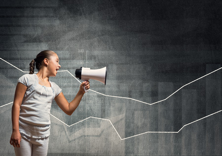Girl of school age with megaphone in empty concrete roomの写真素材
