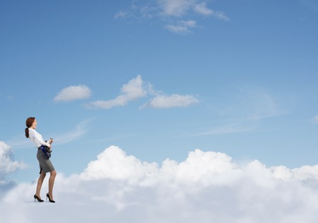 Cheerful businesswoman playing electric guitar standing on cloudの写真素材