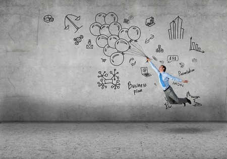 Young successful businessman flying on bunch of drawn balloons on concrete backgroundの写真素材