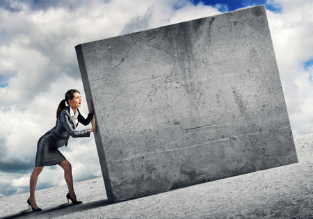 Young businesswoman making effort to move cement wallの写真素材