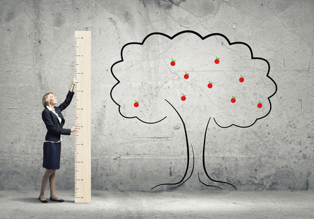 Young businesswoman in suit measuring tree with rulerの写真素材