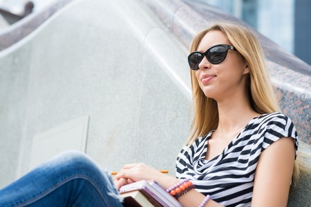 Smiling college student sitting on staircase and studying with booksの写真素材