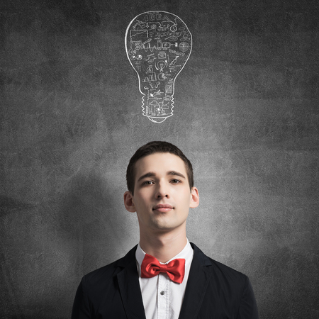 Young man standing in front of chalkboard with light bulb drawn above his headの写真素材