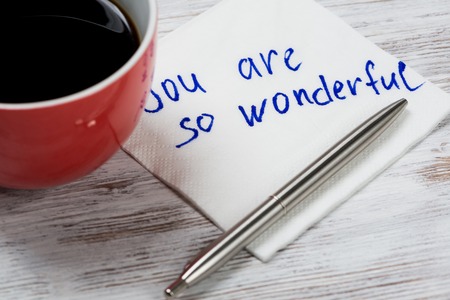 Cup of coffee and napkin with writings on table