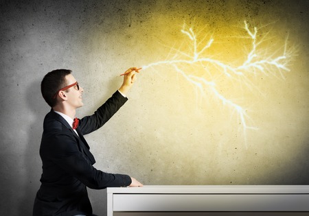 Handsome student sitting at table and drawing on concrete wallの写真素材