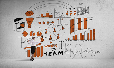 Businesswoman standing with back and drawing business ideas on concrete wallの写真素材