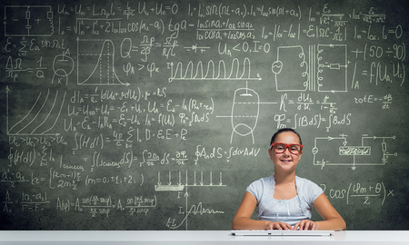 Girl of school age in red glasses sitting at table and typing on keyboardの写真素材
