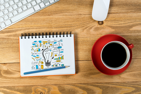 Notepad with idea sketches coffee cup keyboard and pencil on wooden tableの写真素材