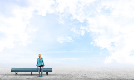 Beautiful girl in hat sitting on bench with book in handsの写真素材