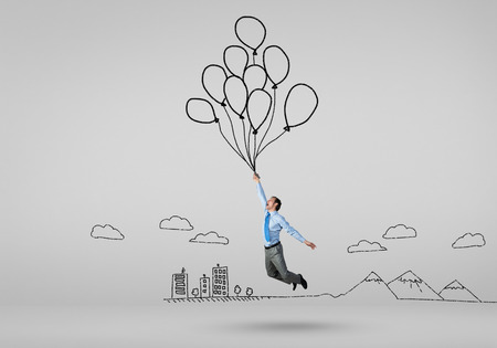 Young successful businessman flies on bunch of drawn balloonsの写真素材