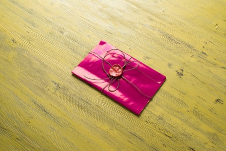 Pink letter envelope with wax seal on wooden surface