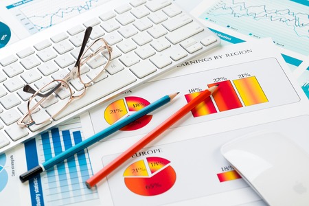 Business workplace with keyboard glasses and financial documents on tableの写真素材