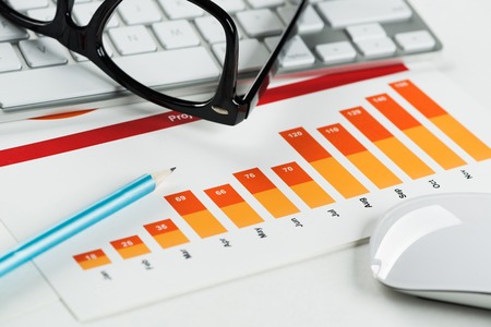 Business workplace with keyboard glasses and financial documents on tableの写真素材
