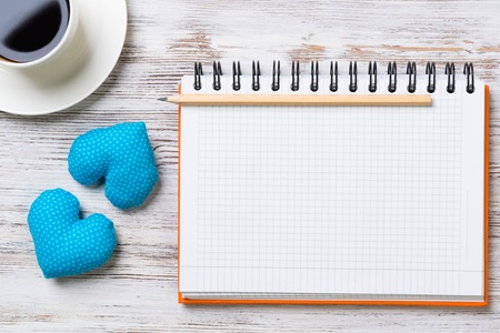 Coffee cup notepad pencil and two hearts on wooden surfaceの写真素材
