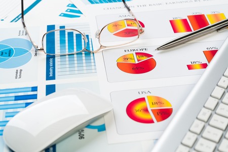 Business workplace with keyboard glasses and financial documents on tableの写真素材