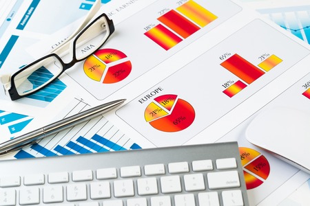 Business workplace with keyboard glasses and financial documents on tableの写真素材