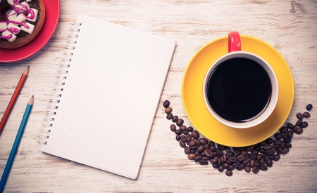 Opened notepad and cup of coffee with donut on wooden table