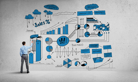 Businessman standing with back and drawing colorful business ideas on concrete wallの写真素材
