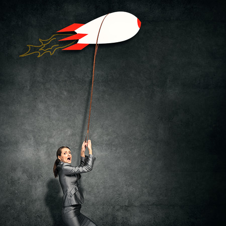 Elegant businesswoman holding drawn rocket on leadの写真素材