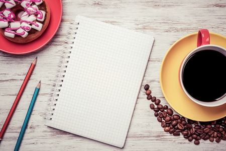 Opened notepad and cup of coffee with donut on wooden tableの写真素材
