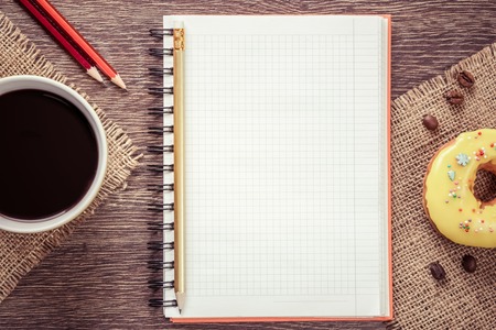 Opened notepad and cup of coffee with donut on wooden table