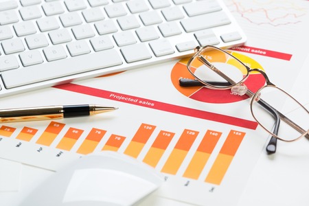 Business workplace with keyboard glasses and financial documents on tableの写真素材