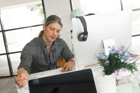 Young man in casual sitting at desk and working on computerの写真素材