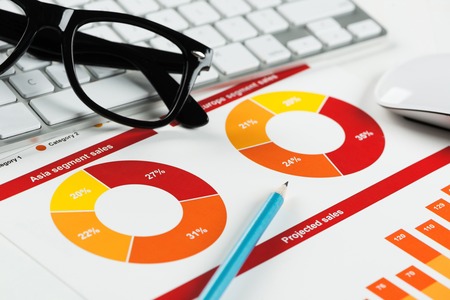 Business workplace with keyboard glasses and financial documents on tableの写真素材