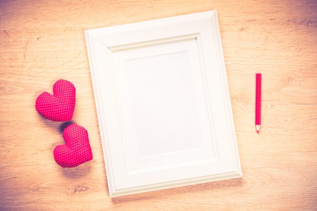 White photo frame small red hearts and pencil on wooden tableの写真素材