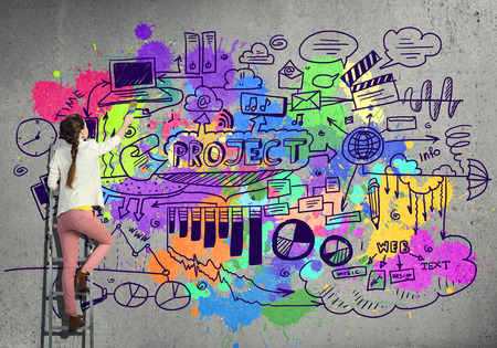 Young woman standing on ladder and painting wallの写真素材