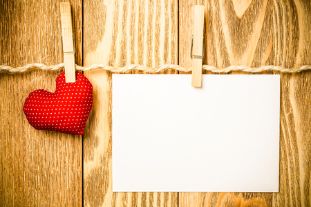 Blank sheet of paper hand made heart pinned to rope on wooden backgroundの写真素材