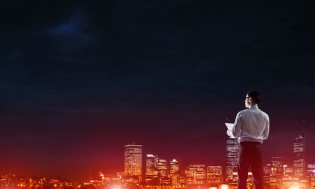 Elegant businessman with suitcase looking at night cityの写真素材