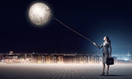Young woman in suit holding moon planet on leadの写真素材