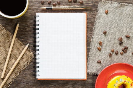 Opened notepad and cup of coffee with donut on wooden table