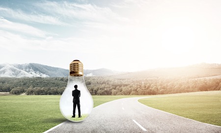 Young businessman trapped inside of light bulb on asphalt roadの写真素材