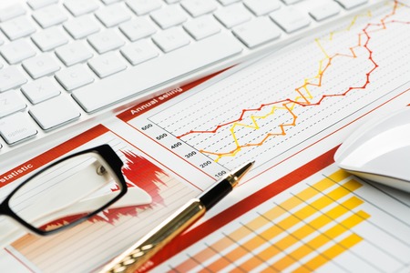 Business workplace with keyboard glasses and financial documents on tableの写真素材