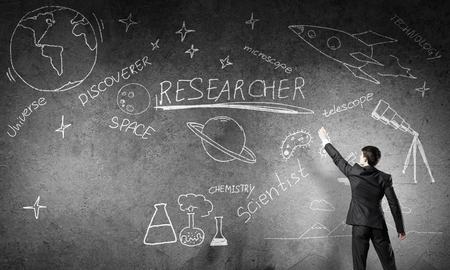 Rear view of man drawing education concept on blackboard with chalkの写真素材